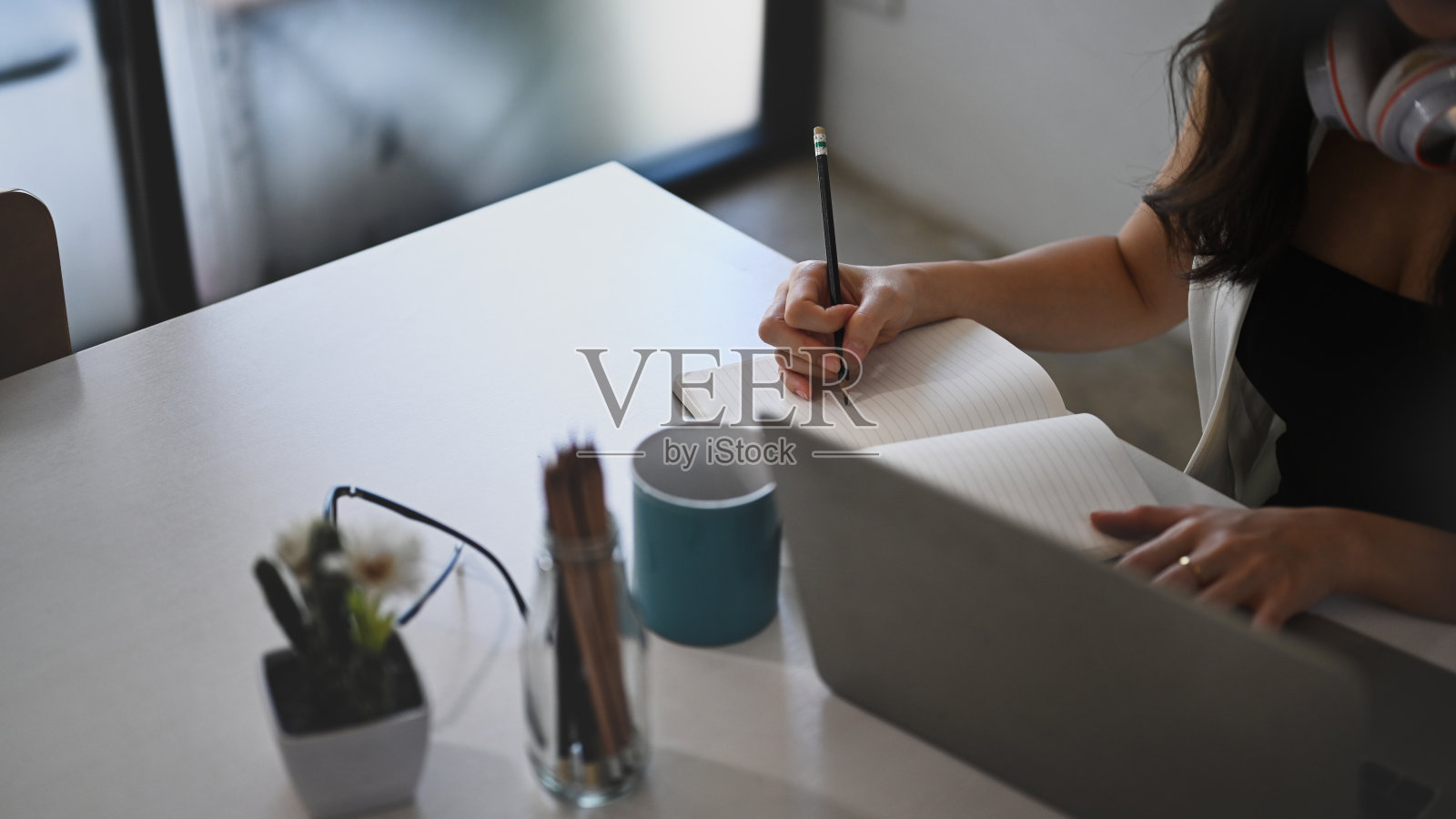 女学生用笔记本电脑在线学习时在笔记本上做笔记的镜头。照片摄影图片