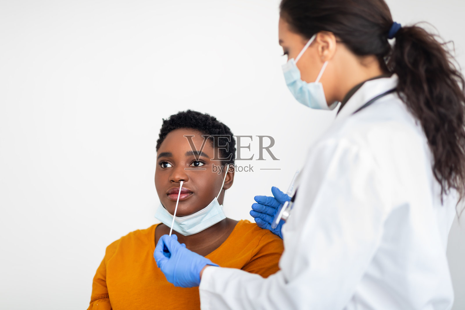专业护士在白人背景下对黑人女性进行Covid-19检测照片摄影图片