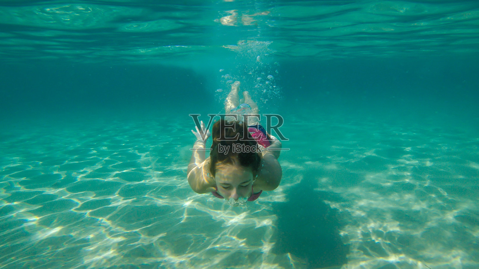 一个女孩在美丽的绿松石水里的沙海底游泳。照片摄影图片