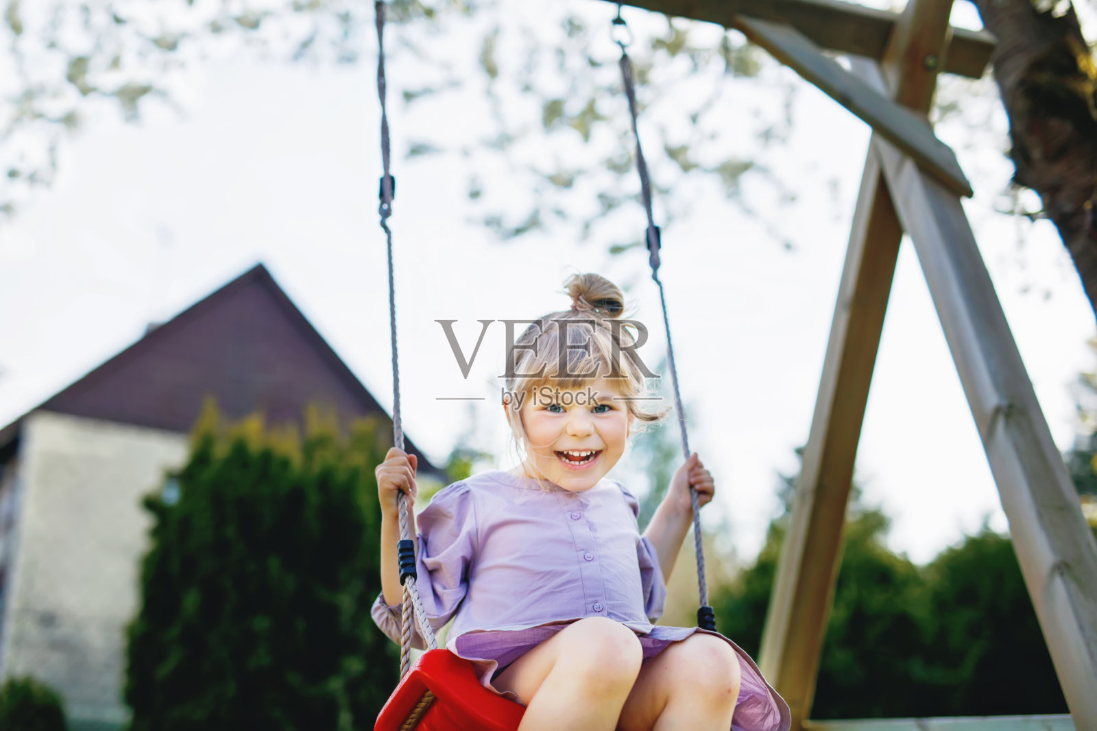 快乐的小女孩在家庭花园的秋千上玩得很开心。微笑积极健康的孩子摆动在阳光灿烂的日子。学前班的女孩又哭又笑。积极的休闲和户外活动。照片摄影图片