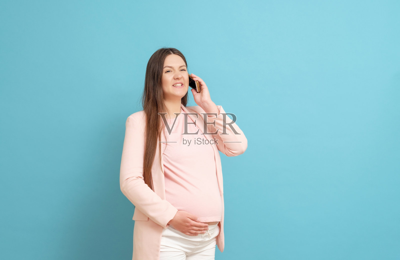 惊恐的年轻孕妇在蓝色背景上被手机呼叫,羊水流出,分娩过程开始照片摄影图片