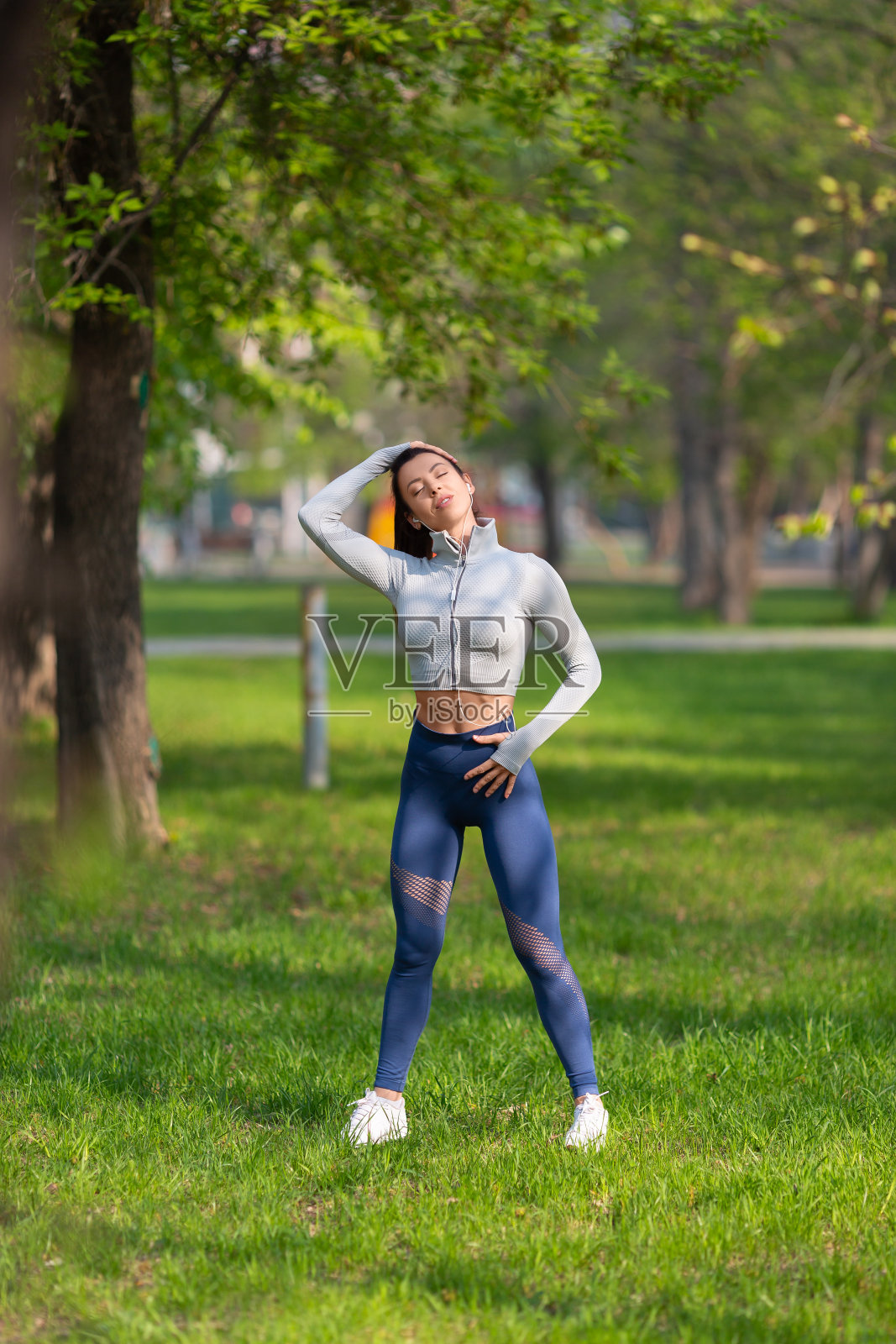 年轻女子伸展颈部——跑步或锻炼前的热身运动。女性跑步者在晨跑前伸展手臂照片摄影图片