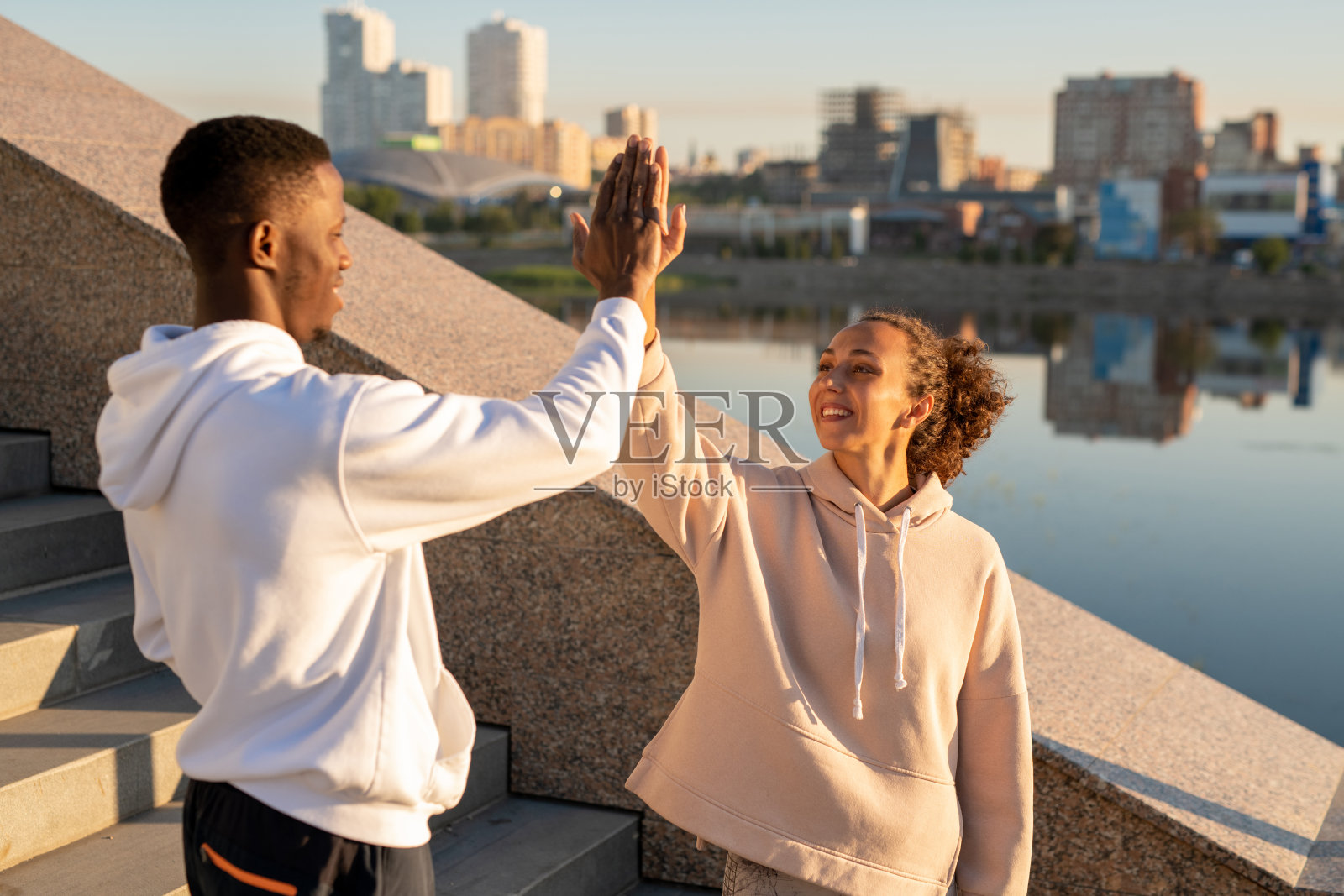 快乐的年轻女性和非洲运动员在帽衫给对方击掌照片摄影图片