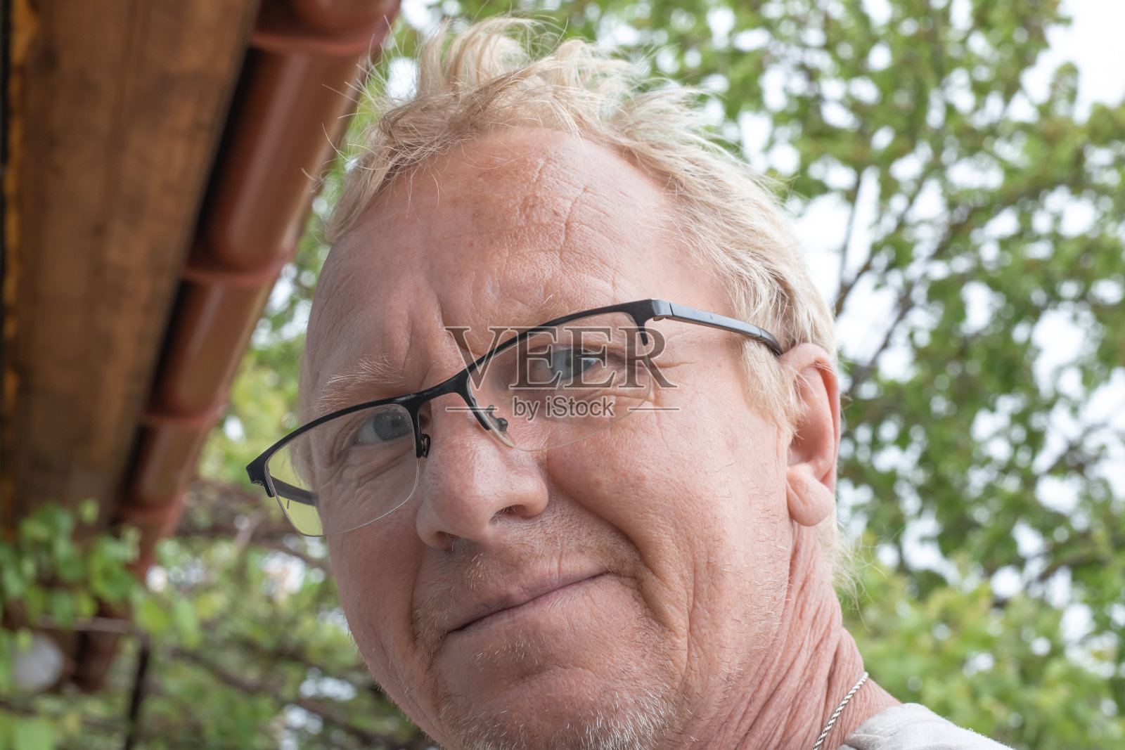 一个长得像欧洲人的成年人,金发,戴着眼镜,在绿树的背景下看着镜头微笑着照片摄影图片