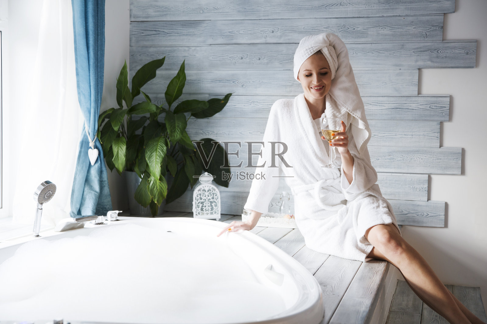 女人穿着浴衣和毛巾在她的头休息浴泡沫和喝葡萄酒。的生活方式。天温泉。照片摄影图片