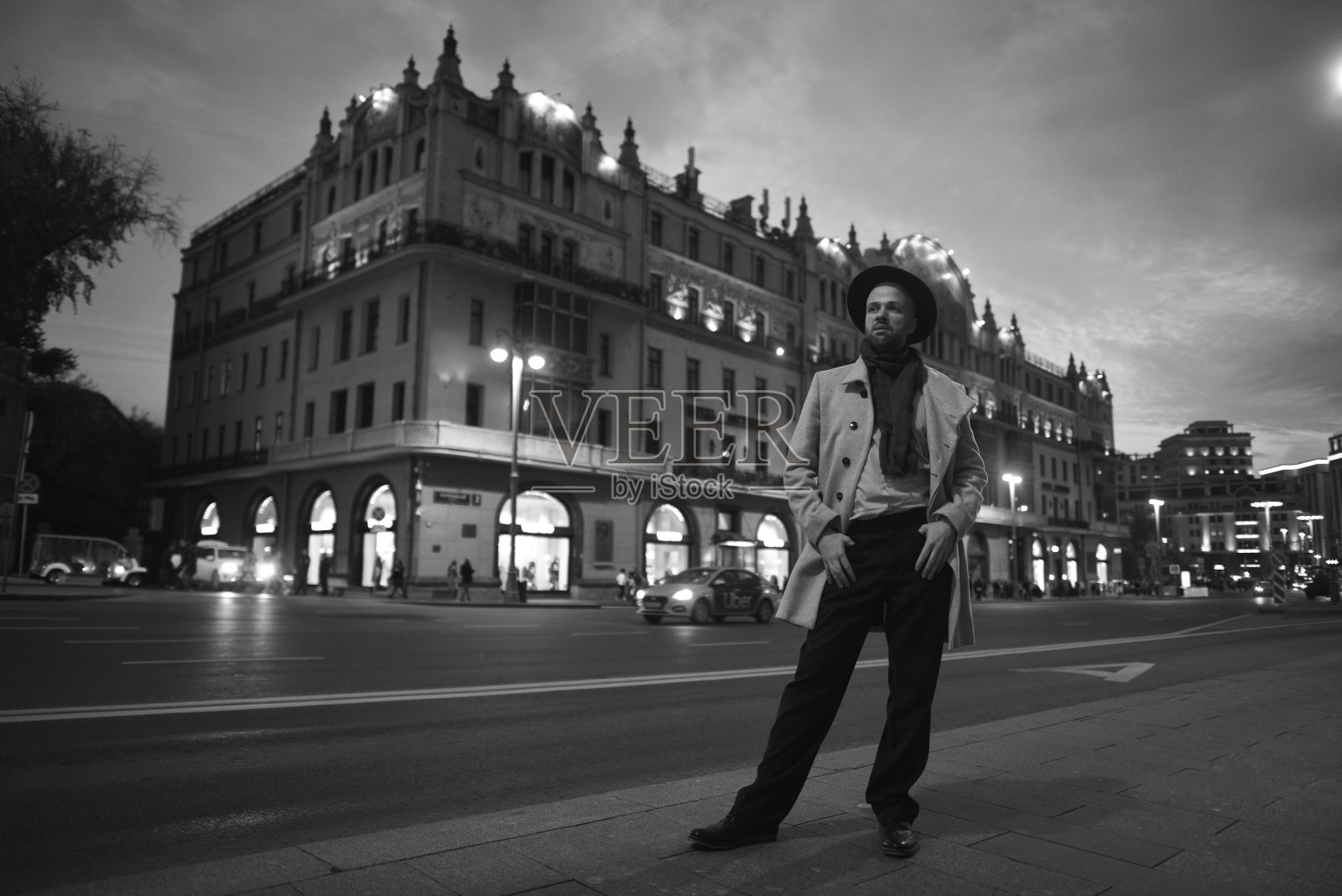 一名俄罗斯男子在莫斯科漫步,用胶片相机拍下他周围的世界。穿着外套,戴着帽子的时髦男人。模糊的背景。黑白人像。夜晚城市的灯光照片摄影图片