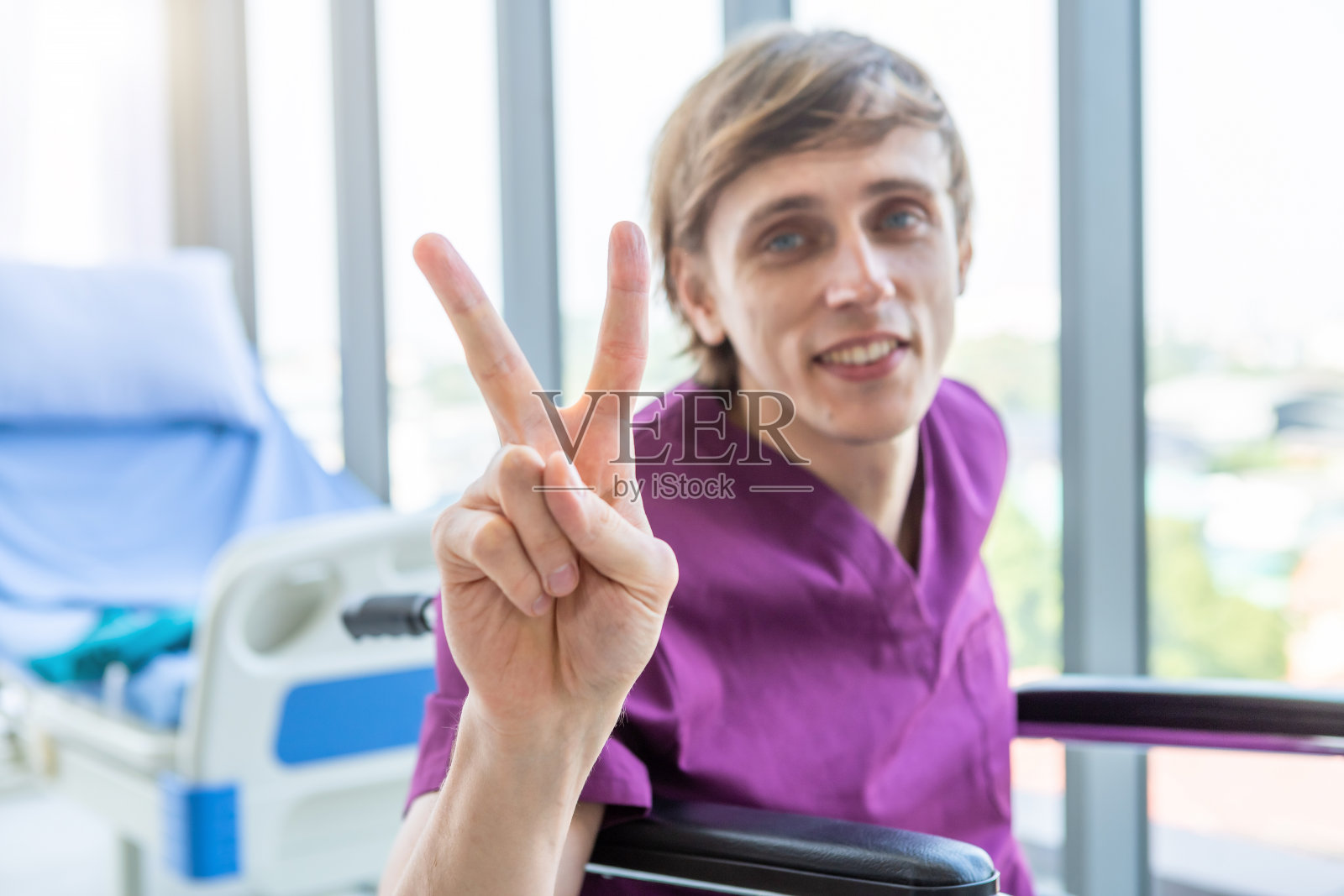 一个男人病人坐在轮椅上抽象模糊的焦点显示举起两个手指与疾病斗争起来的笑脸在医院背景很好的症状。照片摄影图片