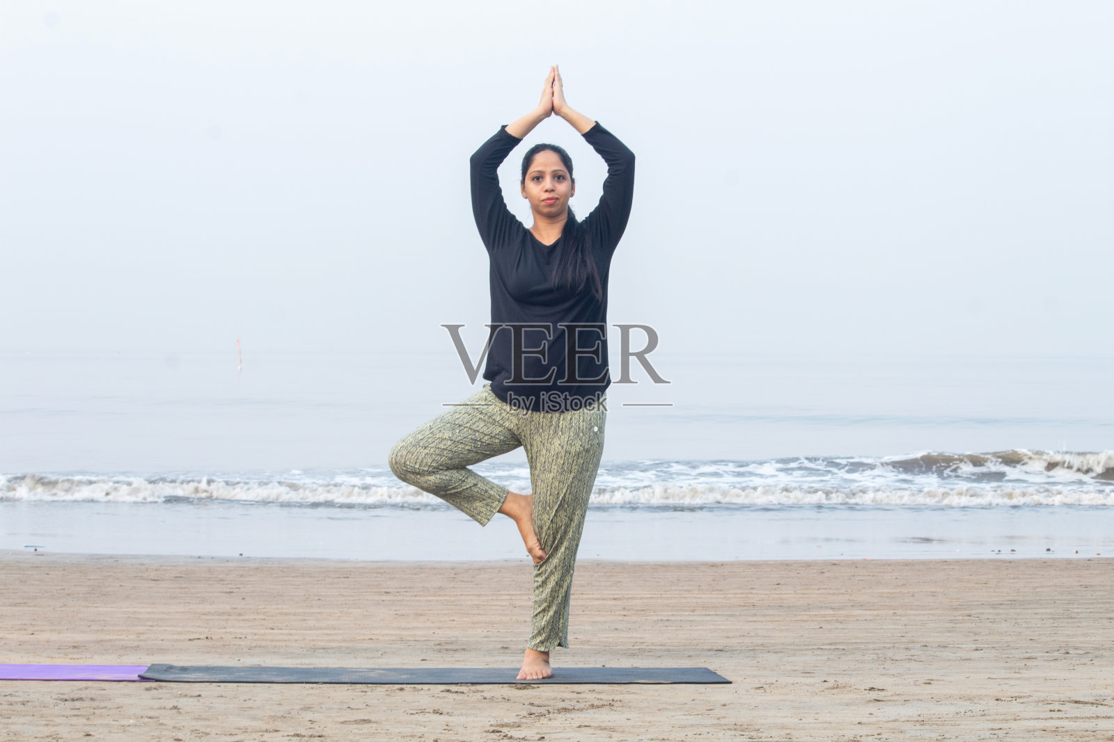 在海滩上练习瑜伽树姿势的女人照片摄影图片