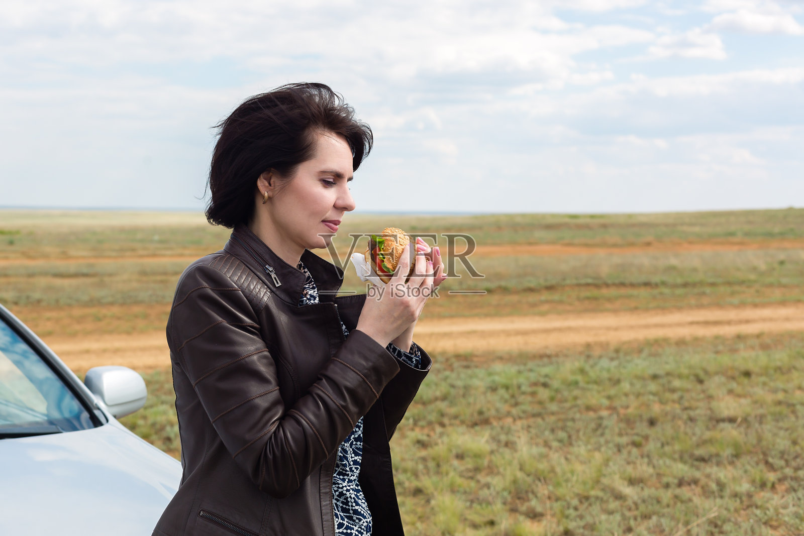 在自然界中,一个手里拿着玻璃杯的女人将要吃一个汉堡包照片摄影图片