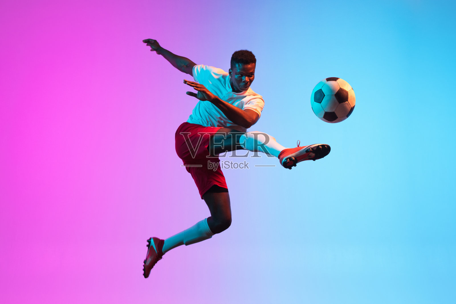 一个非洲人,职业足球运动员,在霓虹灯的渐变蓝粉色背景下孤立训练。照片摄影图片
