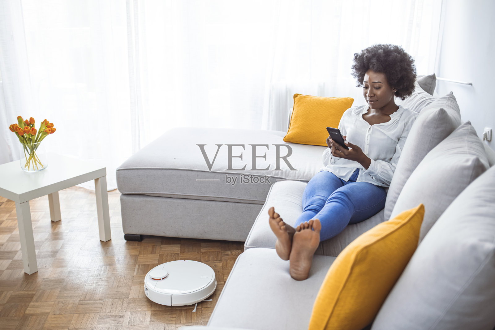 当女人在沙发上休息时,机器人真空吸尘器正在打扫房间。照片摄影图片