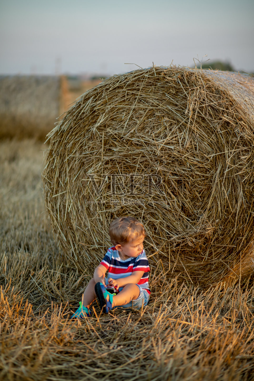 一个小男孩坐在农场上,背景是收获季节的干草照片摄影图片