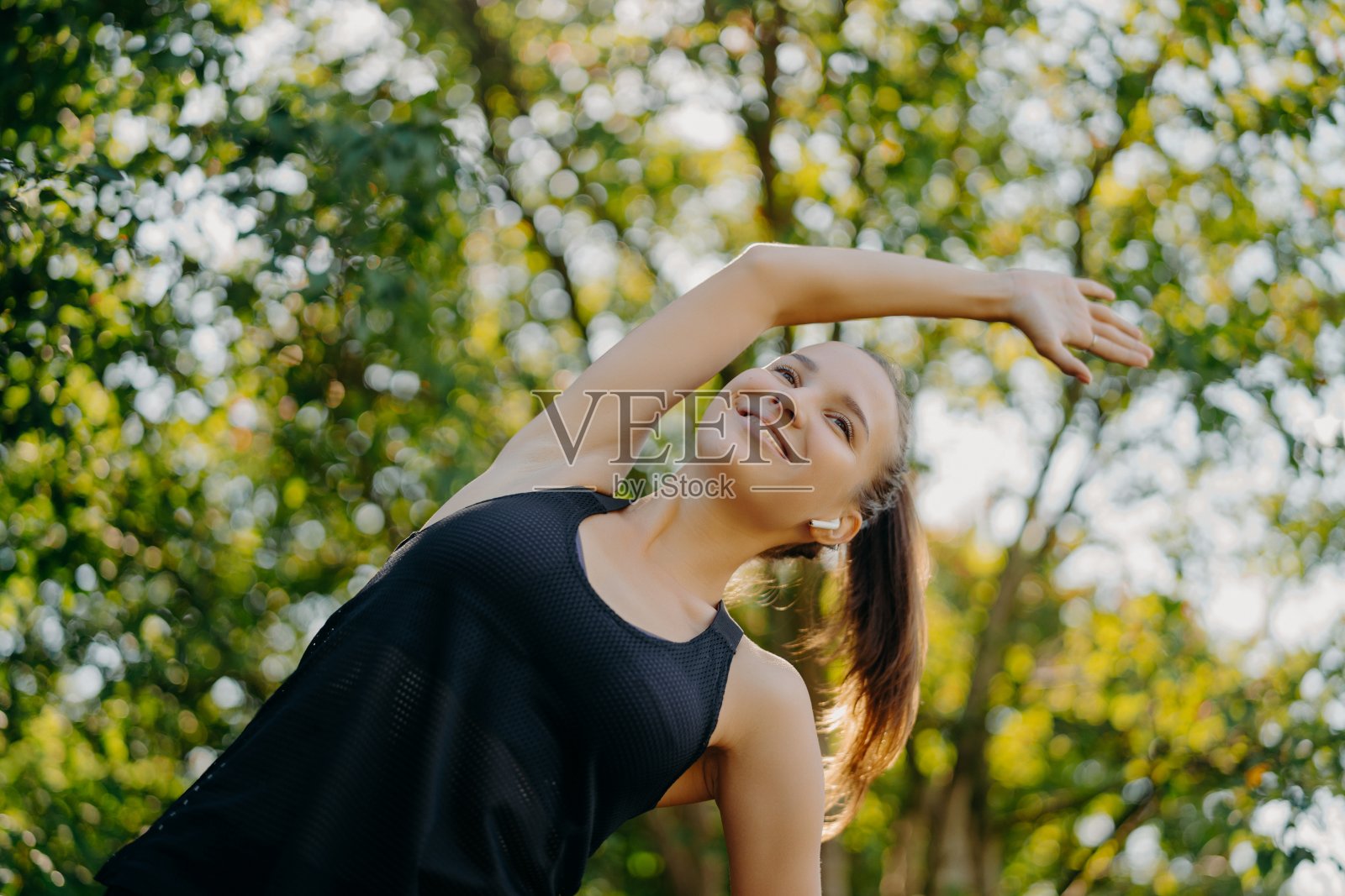 运动健身妇女做热身和伸展运动,侧身有内容的面部表情穿着活跃的穿着姿势,在夏季的背景下对自然。运动和动力照片摄影图片