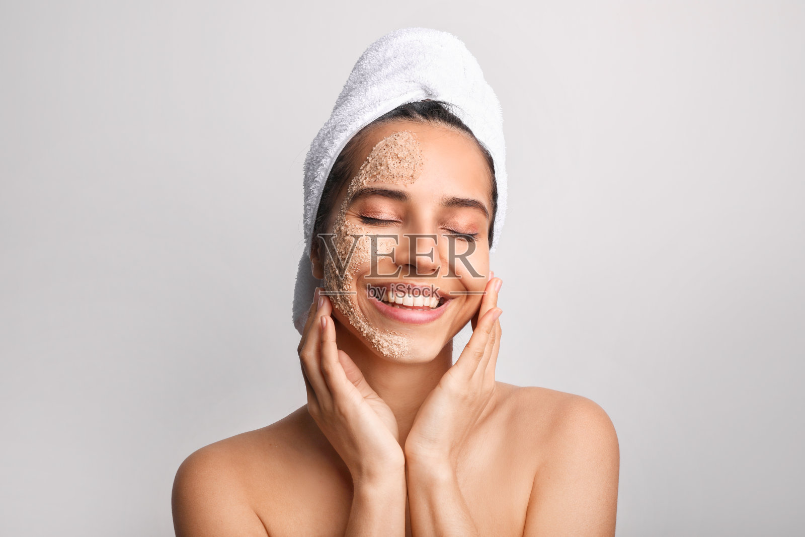 美丽的女人在白色的背景下用磨砂膏擦脸照片摄影图片