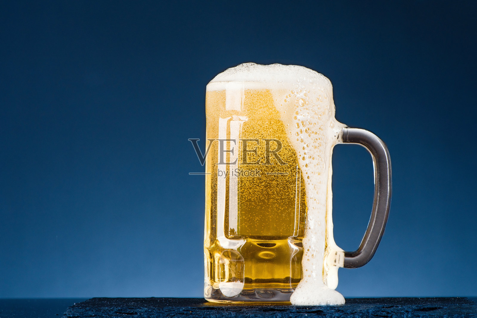 一杯在蓝色背景上冒着泡沫的啤酒。照片摄影图片