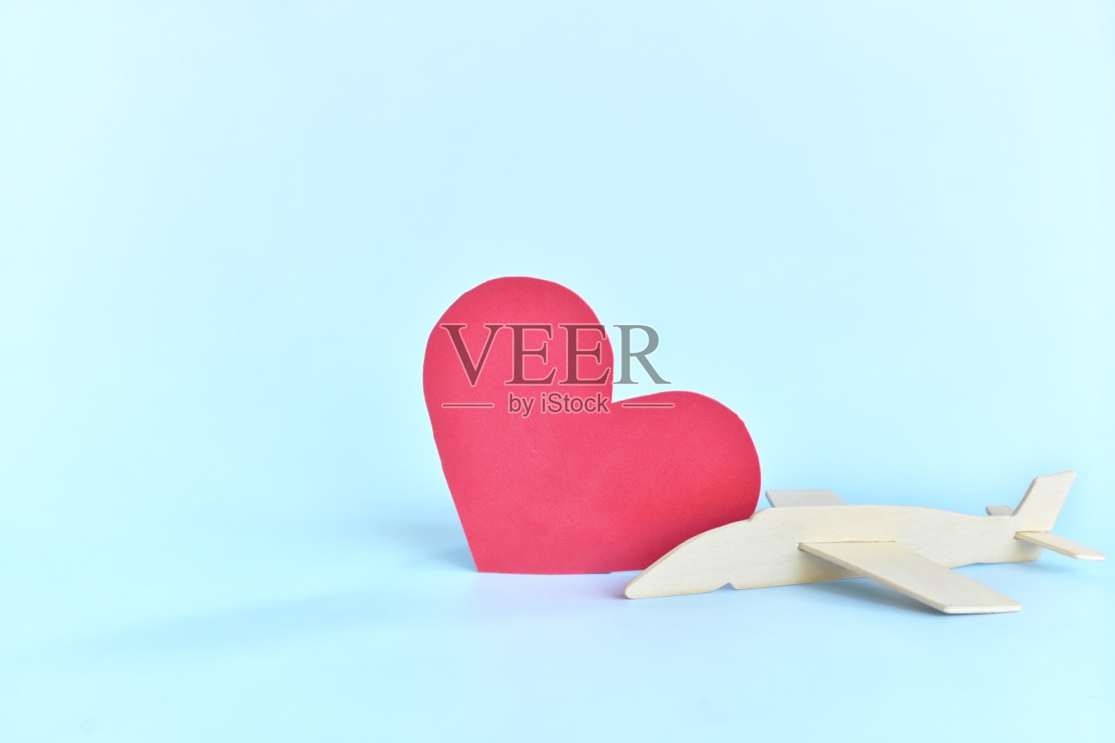木制飞机模型旁边的红色心形在天空蓝色的背景。喜欢旅游和度假的概念。照片摄影图片