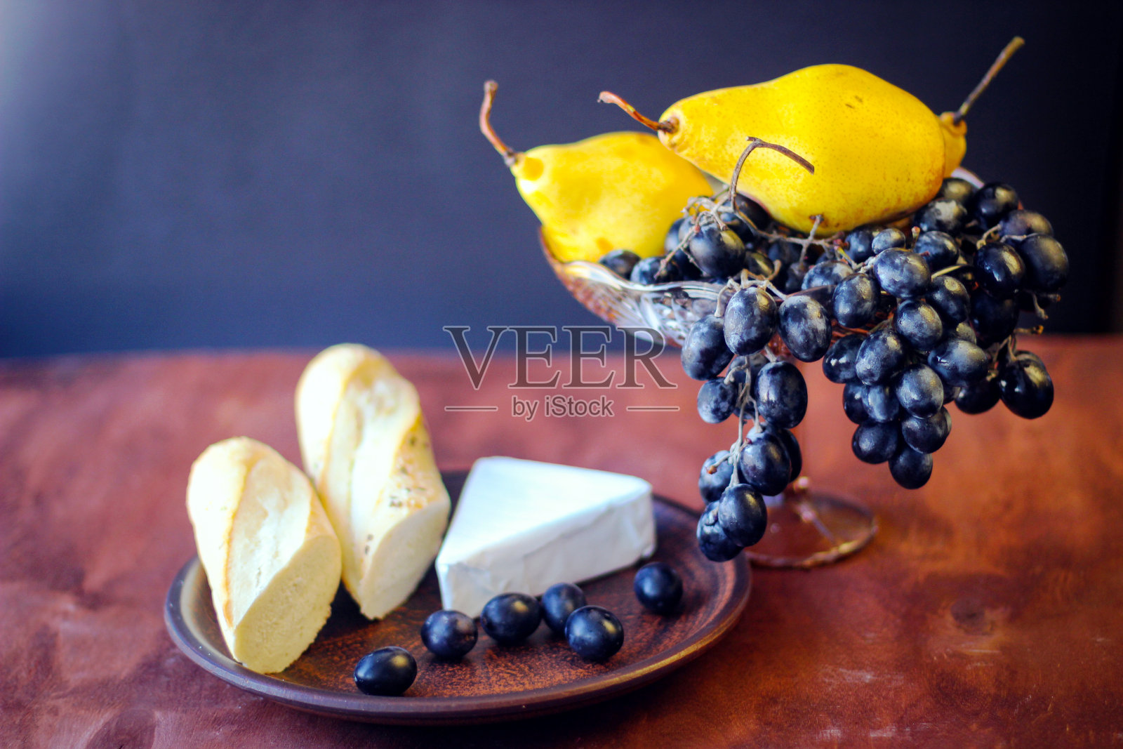 美妙的食物:黑色的葡萄刷,一片布里干酪,两片法棍面包和一些成熟的黄梨照片摄影图片