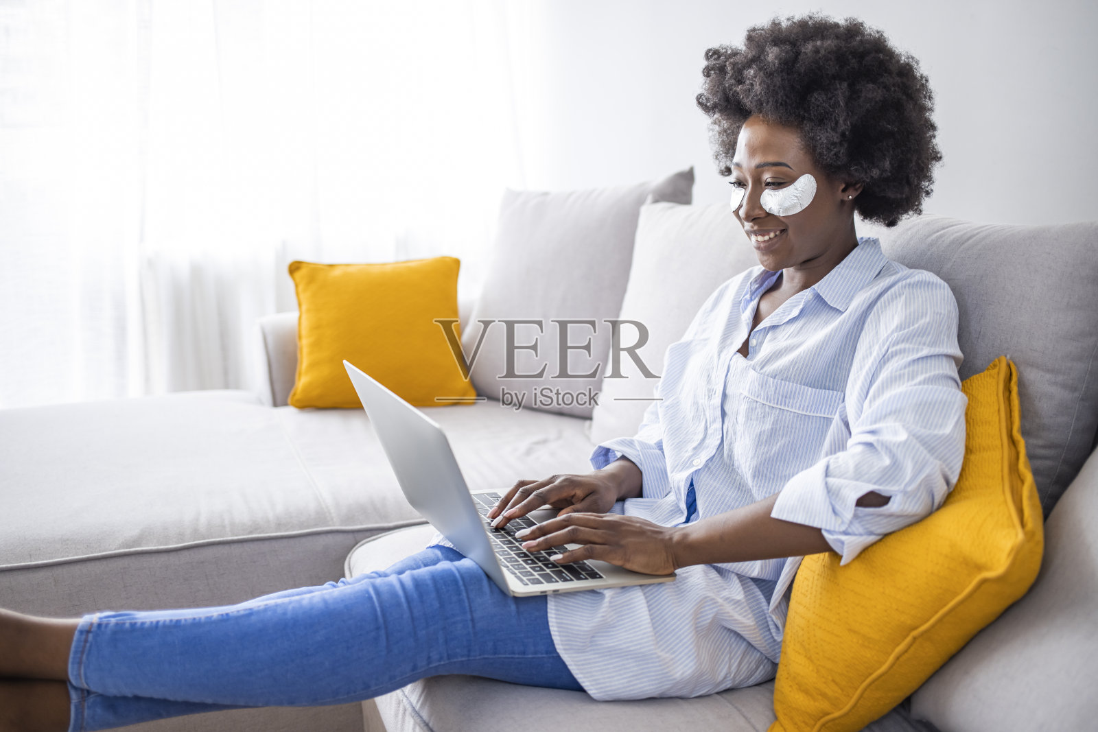 快乐的女性坐在沙发上,穿着小路,同时使用笔记本电脑和智能手机照片摄影图片