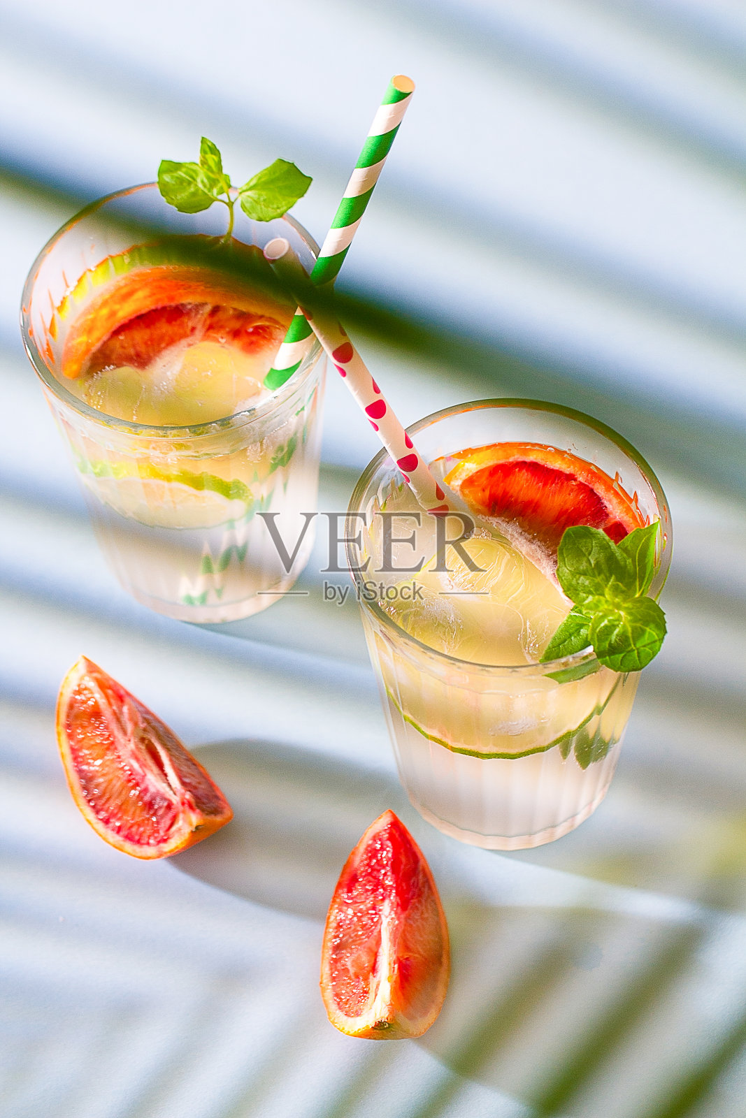 蓝色的桌子上放着两杯清凉的夏日柠檬水,加冰、柠檬片、红橙和薄荷枝。夏季饮料。俯视图照片摄影图片