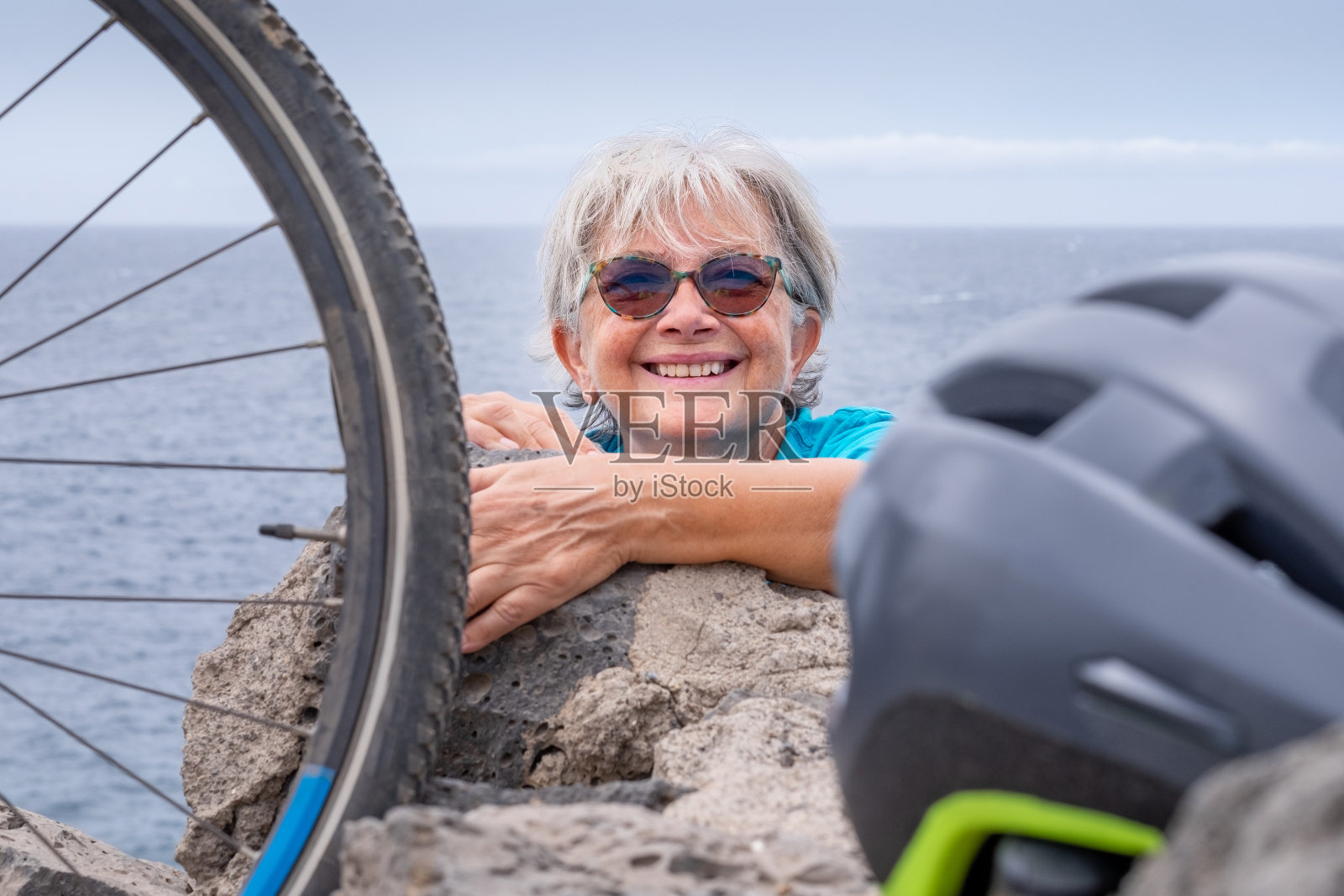 一位骑自行车的妇女骑着她的电动自行车徒步旅行后,她的头从岩石中探了出来。成熟女人笑得开心照片摄影图片