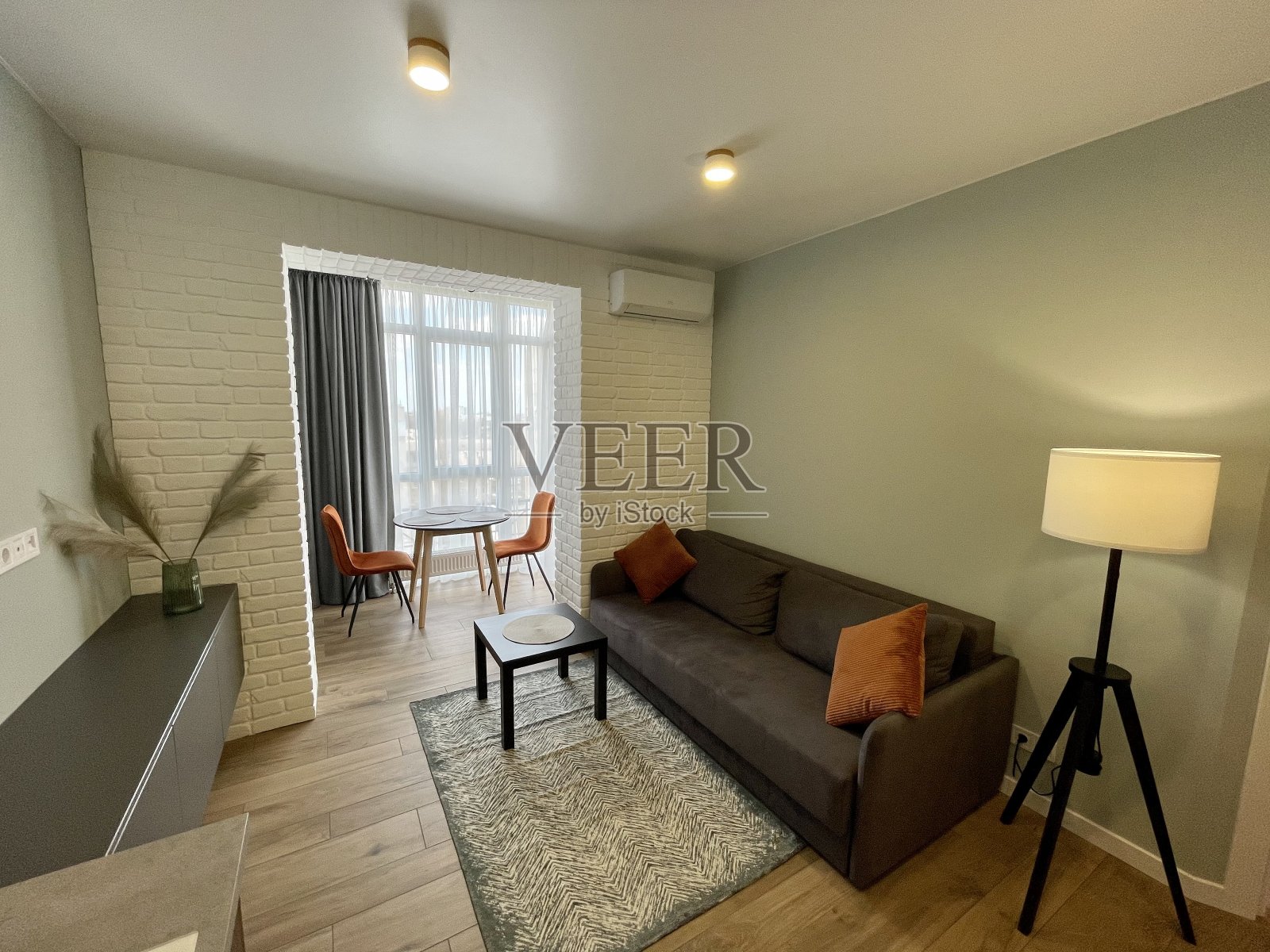 现代的客厅,浅色的墙壁和木地板,灰色的沙发和橙色的靠垫,橙色的椅子和一个靠窗的桌子照片摄影图片