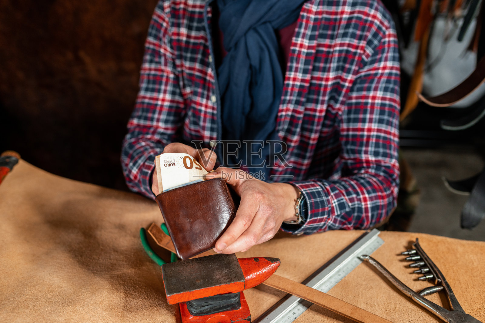 一个面目全非的男人坐在他的车间里从钱包里拿出钱。照片摄影图片