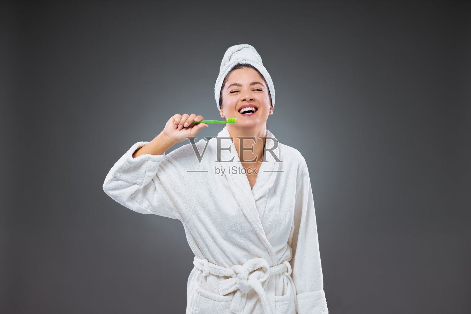 刷牙和口腔护理。一个穿着浴袍、头裹毛巾、面带微笑的女孩,手里拿着牙刷在刷牙照片摄影图片