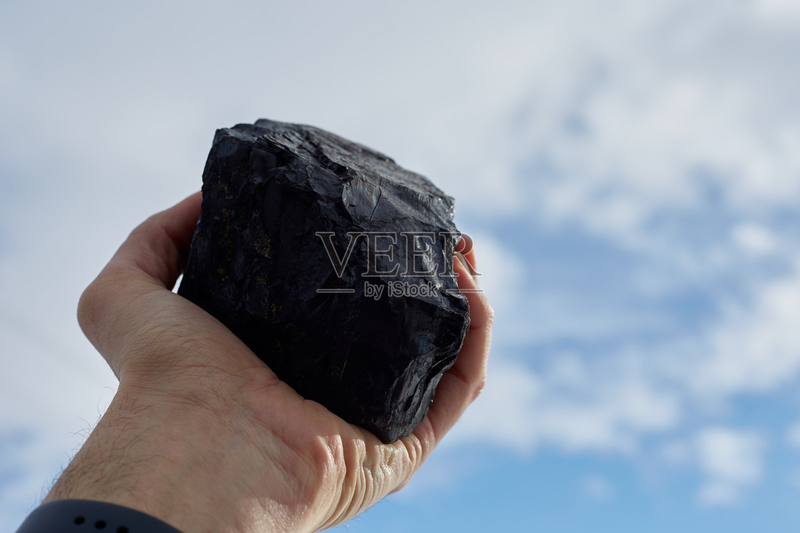 一个男人手里拿着煤,对抗着蓝天和空气污染照片摄影图片