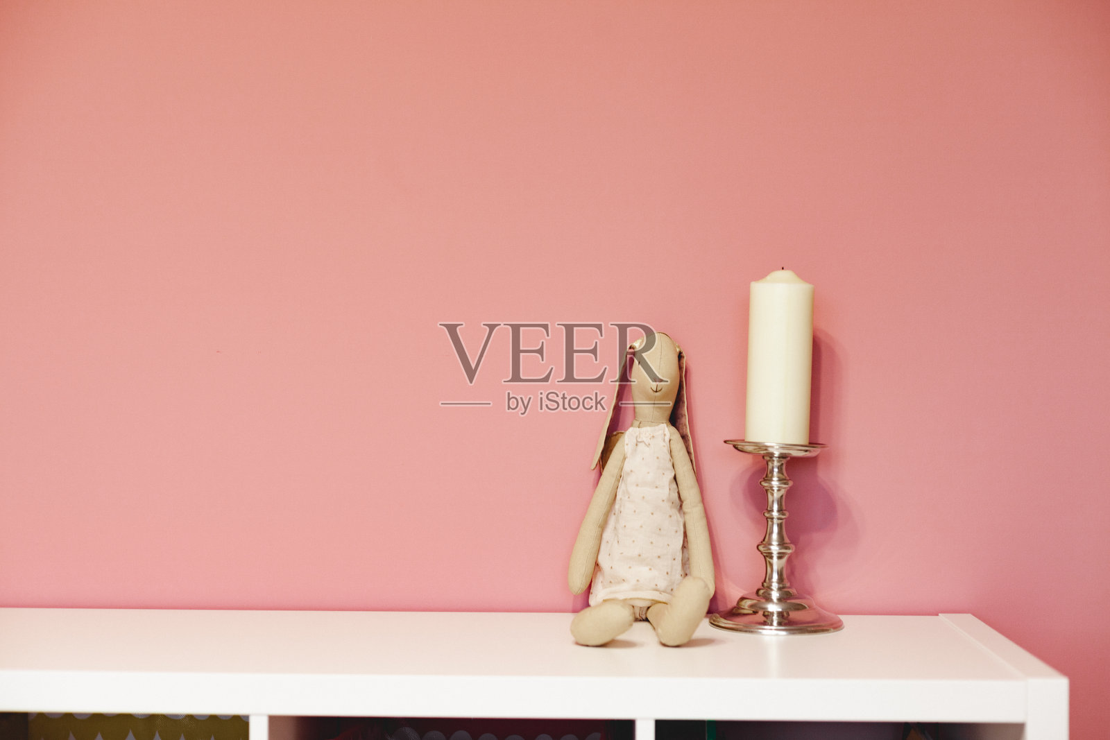 Сloth粉色墙边白色架子上的银色烛台上的玩具兔子和蜡烛照片摄影图片