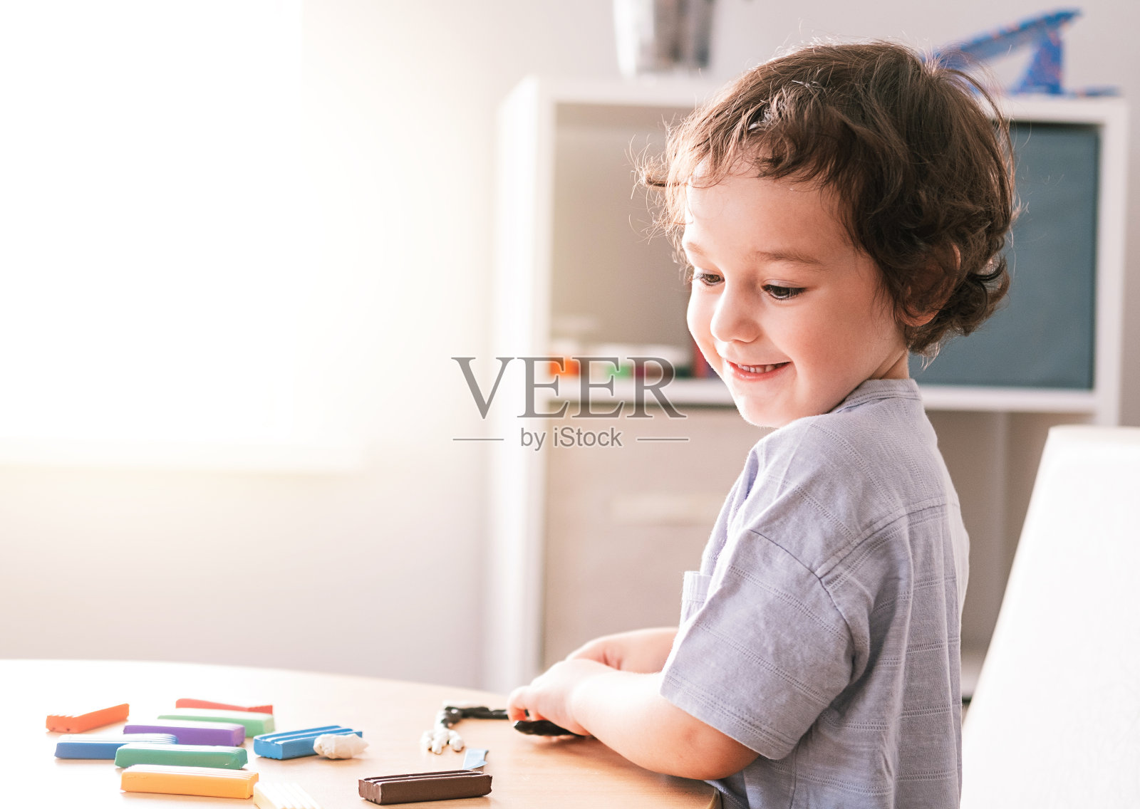 快乐的小男孩坐在桌旁用橡皮泥雕刻。照片摄影图片