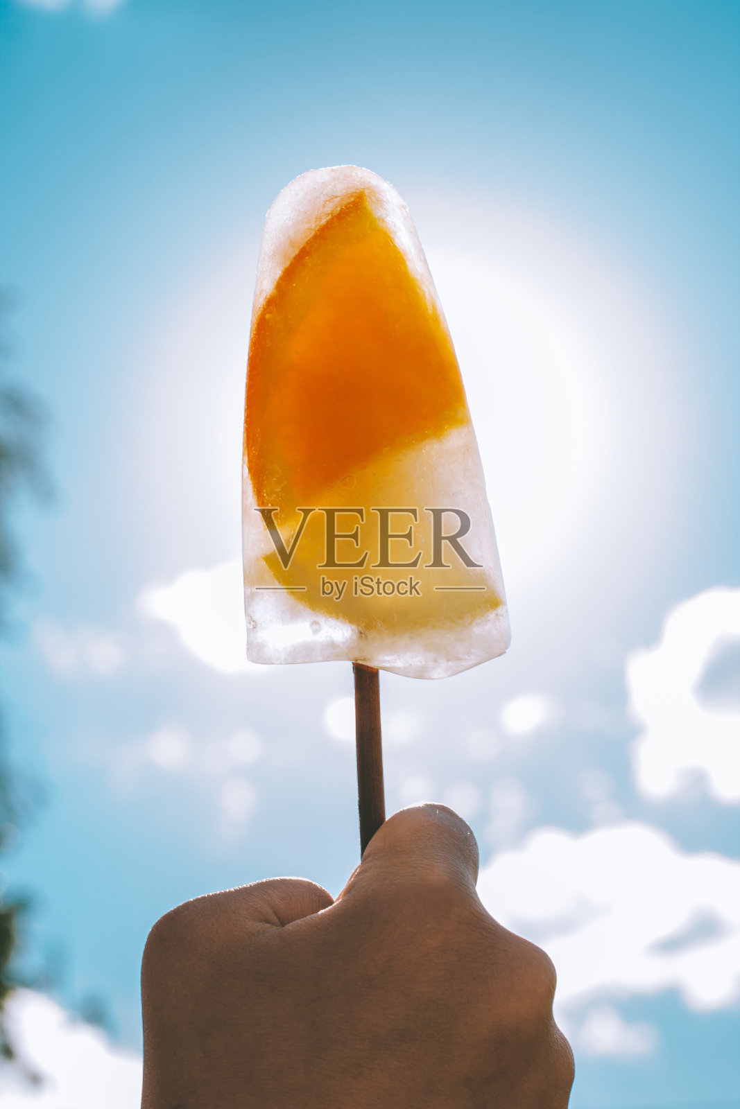 在蓝天的背景下,孩子手中的棒冰。冰淇淋用橙子和柠檬片,垂直排列照片摄影图片