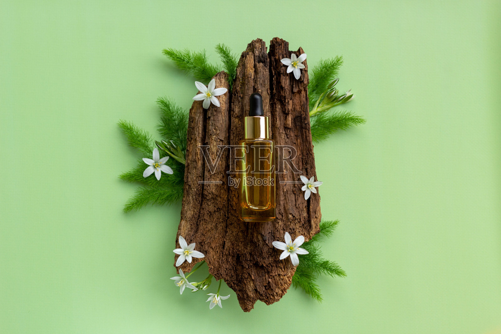由天然的树皮和盛开的花朵上的精油瓶组成。照片摄影图片