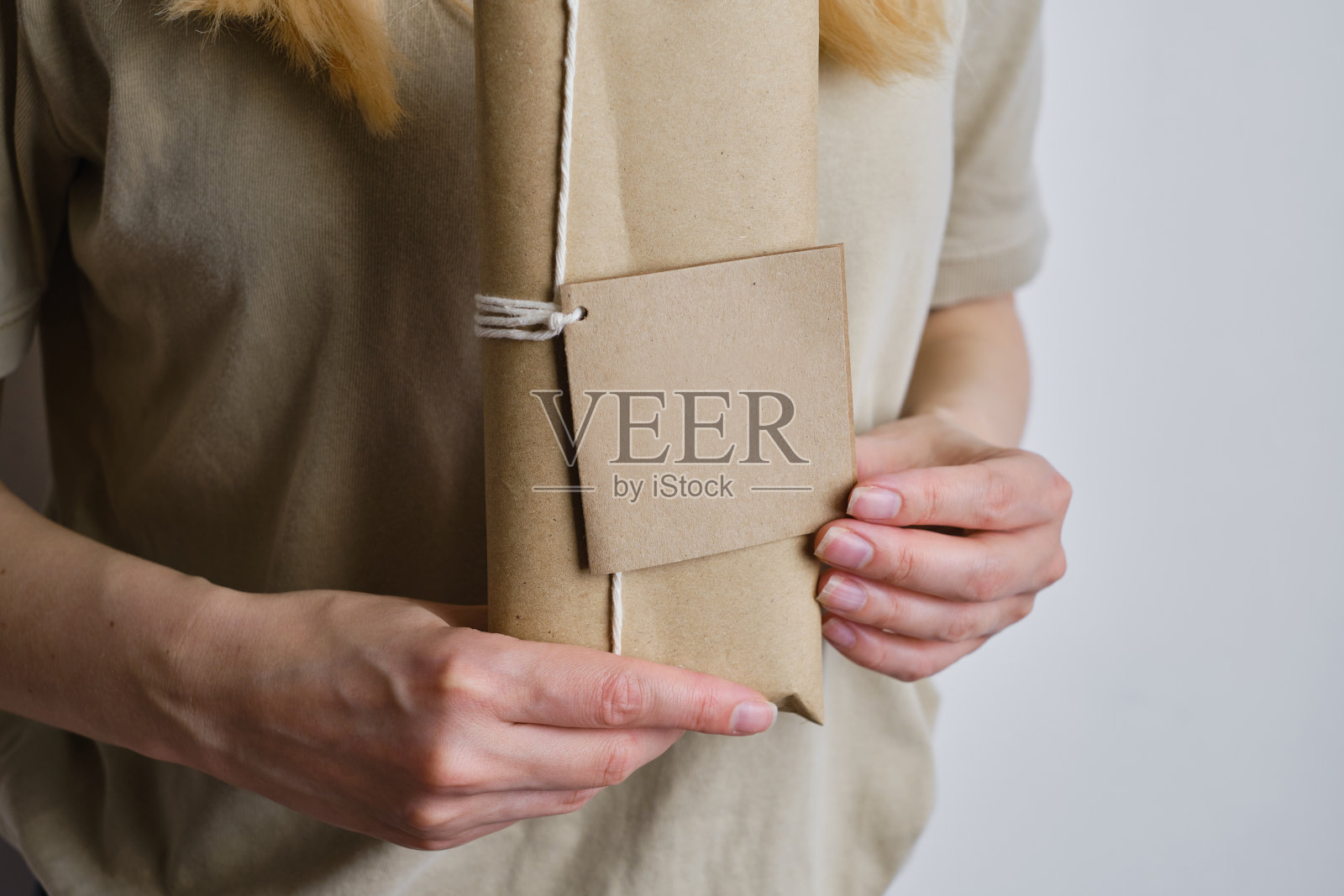 女人手里拿着一个纸盒,上面写着一张祝贺卡片。牛皮纸包装。空包装,空空间。盒子特写。送货服务。在纸上留下留言或邀请的空白处照片摄影图片