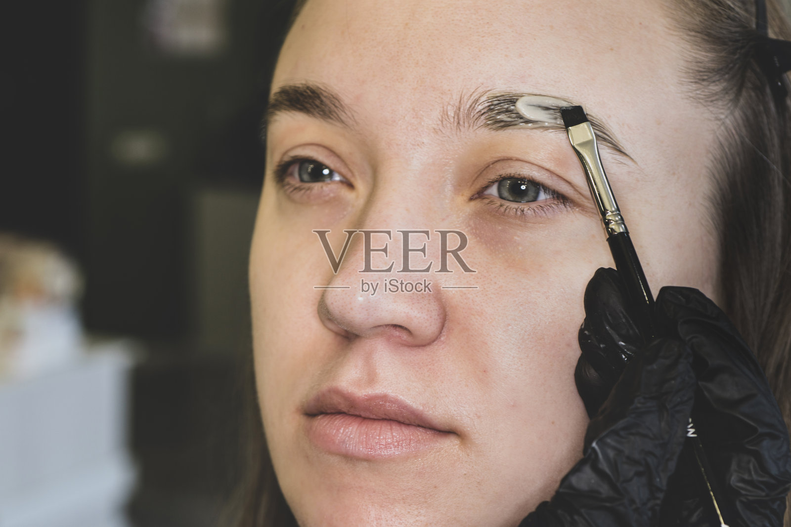 染眉毛是一种美容方法。美容师在美眉水疗期间用深棕色的化妆品补眉的特写照片摄影图片