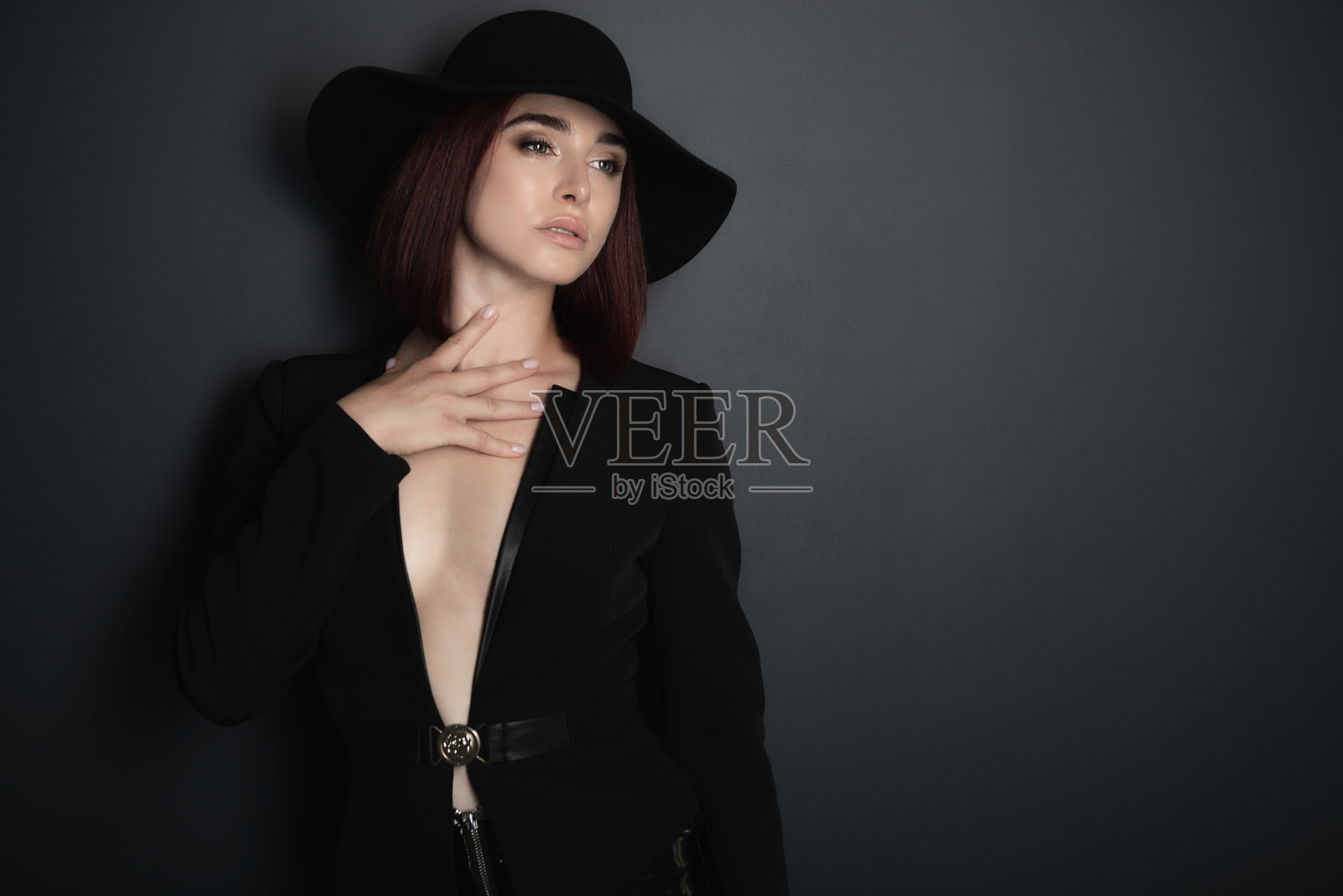 美丽的时尚女人与完美的身体。肖像美丽的女孩穿着黑色外套,乳胶紧身裤和帽子摆姿势在工作室在深灰色的背景照片摄影图片