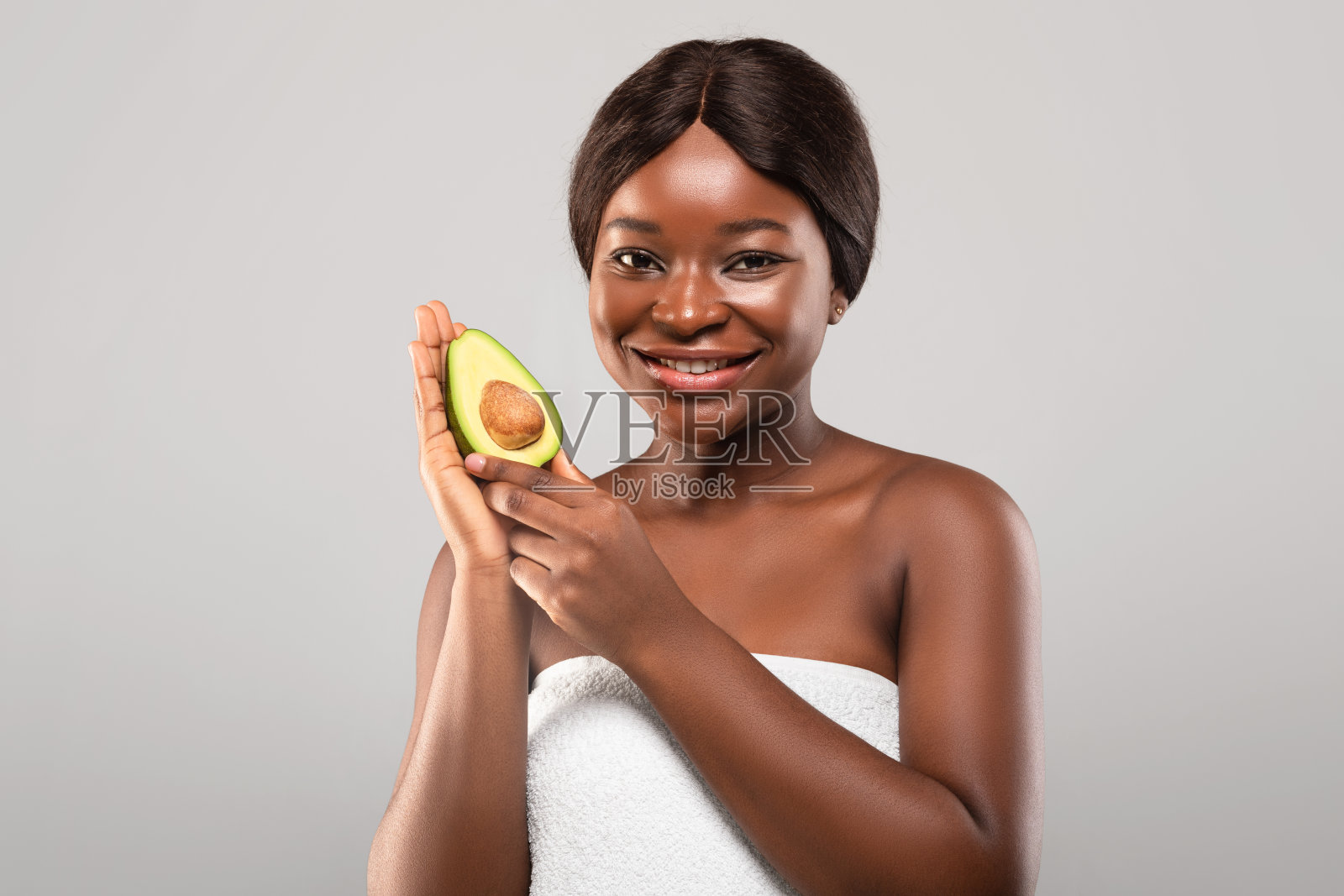迷人的黑色女性包裹在毛巾摆姿势与鳄梨半手照片摄影图片
