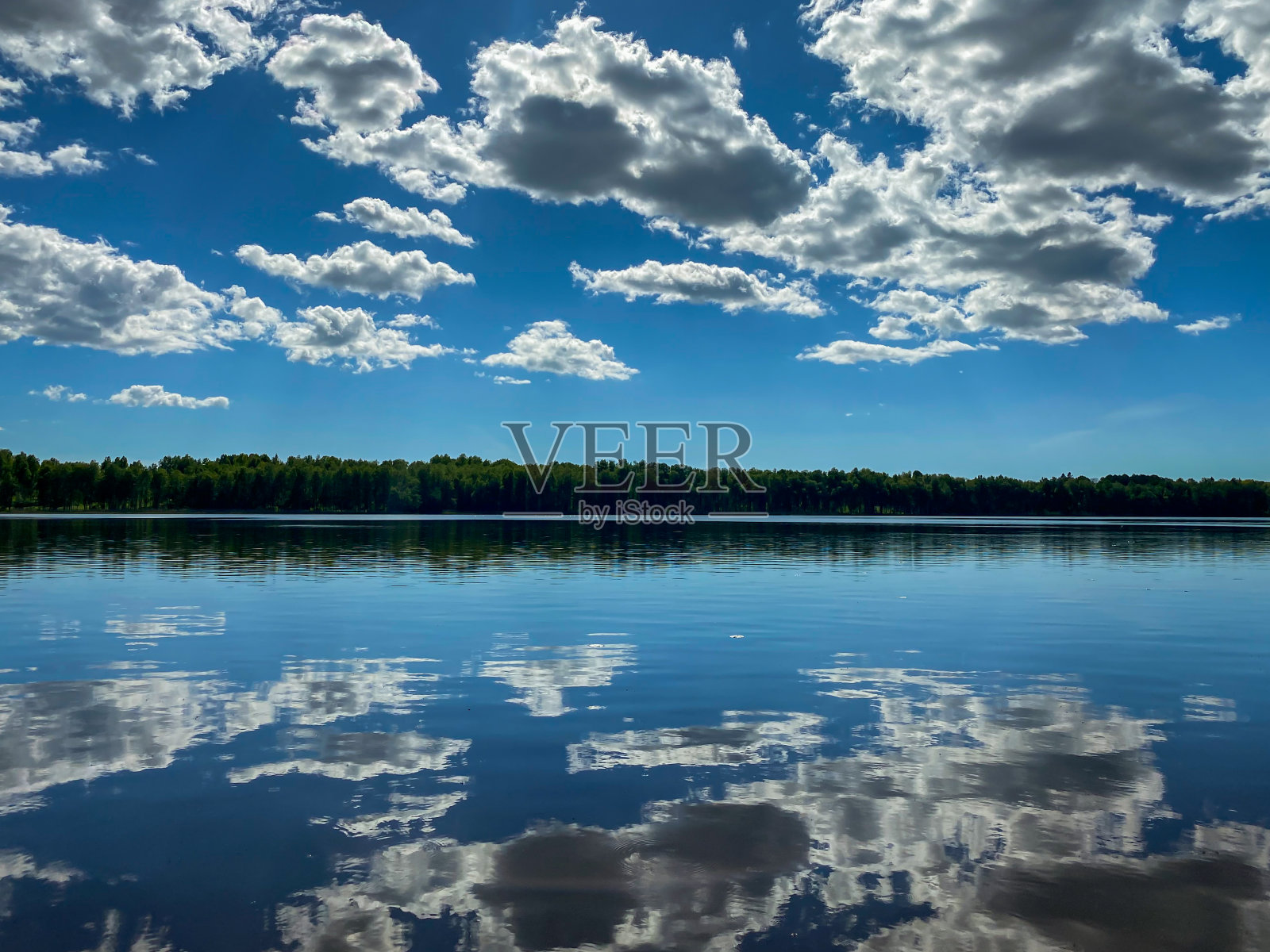 美丽的夏季景观,白色的积云倒映在平静的蓝色湖水。照片摄影图片
