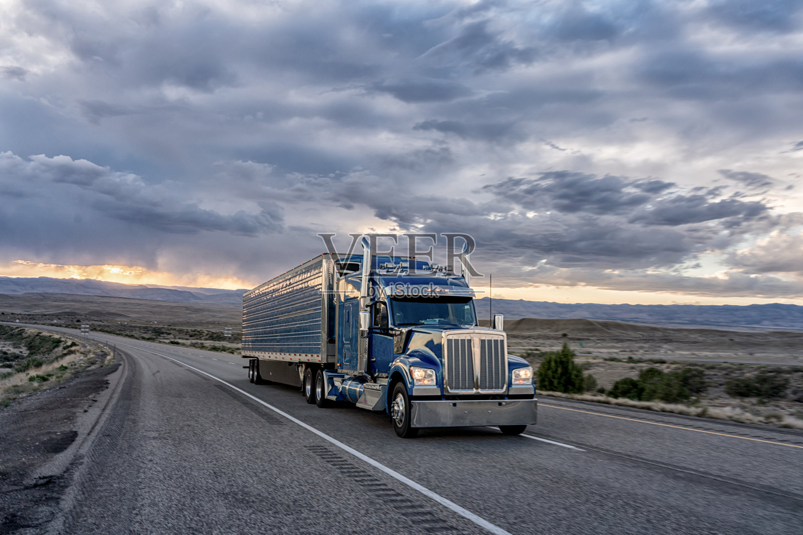 一辆大型商业货运半挂车在沙漠公路上向东行驶,以交付货物,一个戏剧性的日落背景照片摄影图片