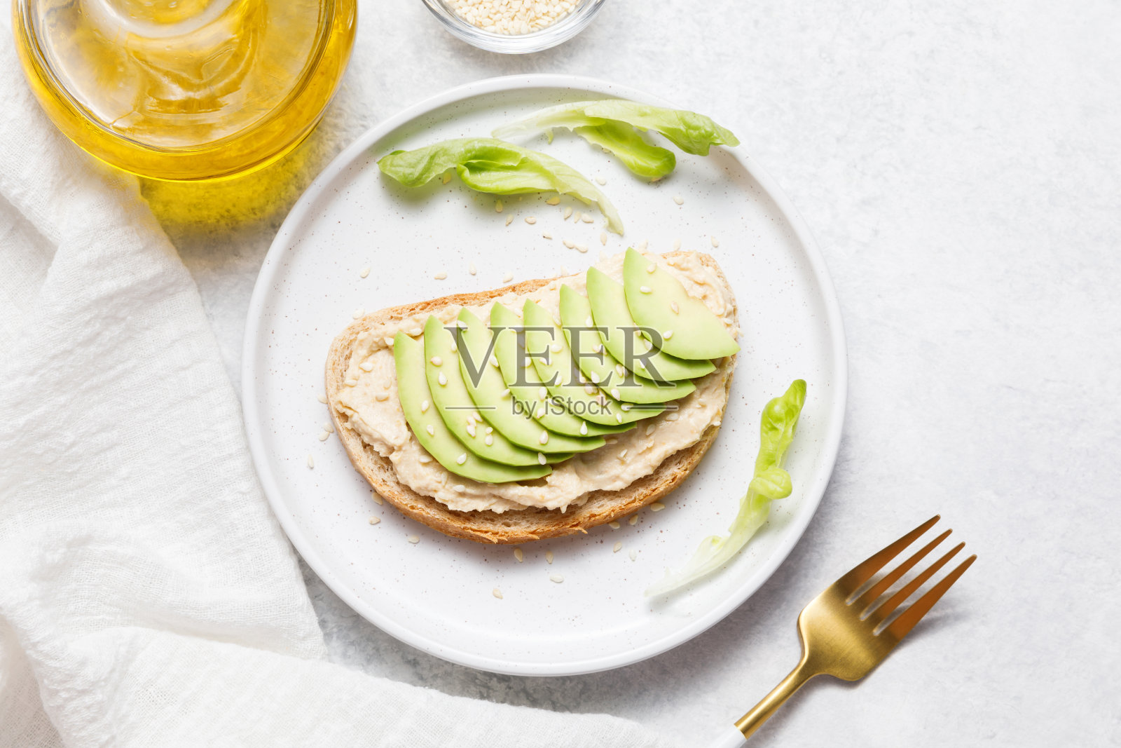 糠面包吐司配鹰嘴豆、鹰嘴豆泥和鳄梨在白色的石头桌子上。照片摄影图片