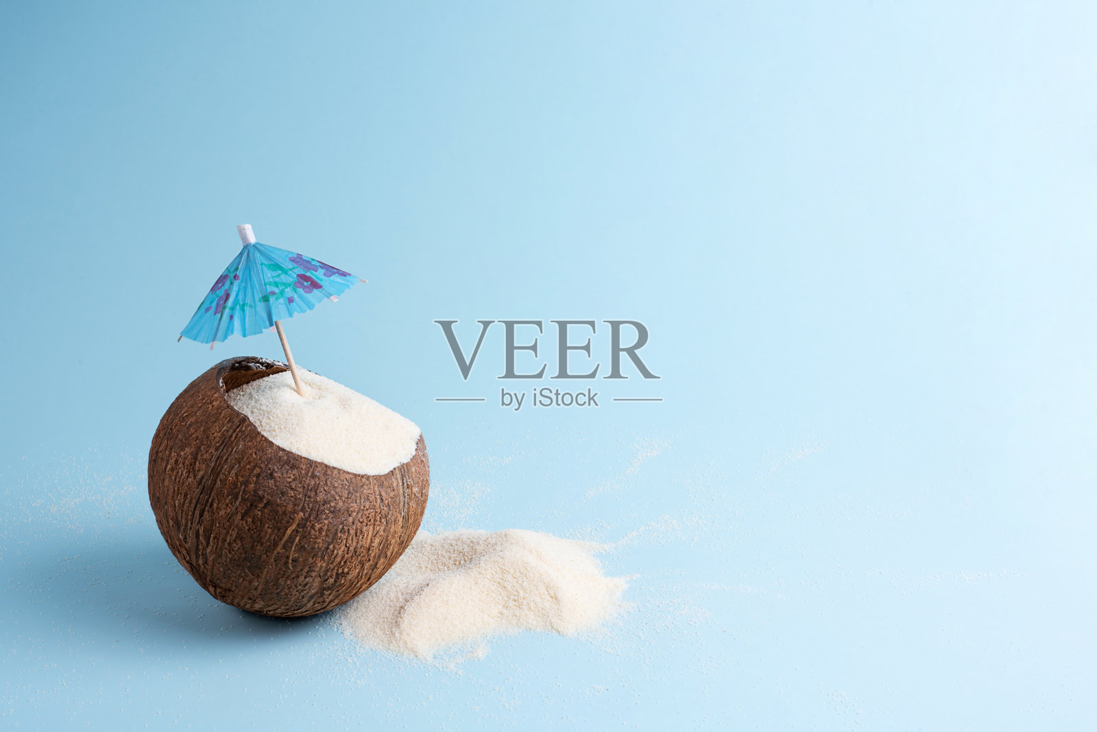 近距离的椰子与倒出的沙子和鸡尾酒伞在一个蓝色的背景,海滩夏季度假概念。照片摄影图片