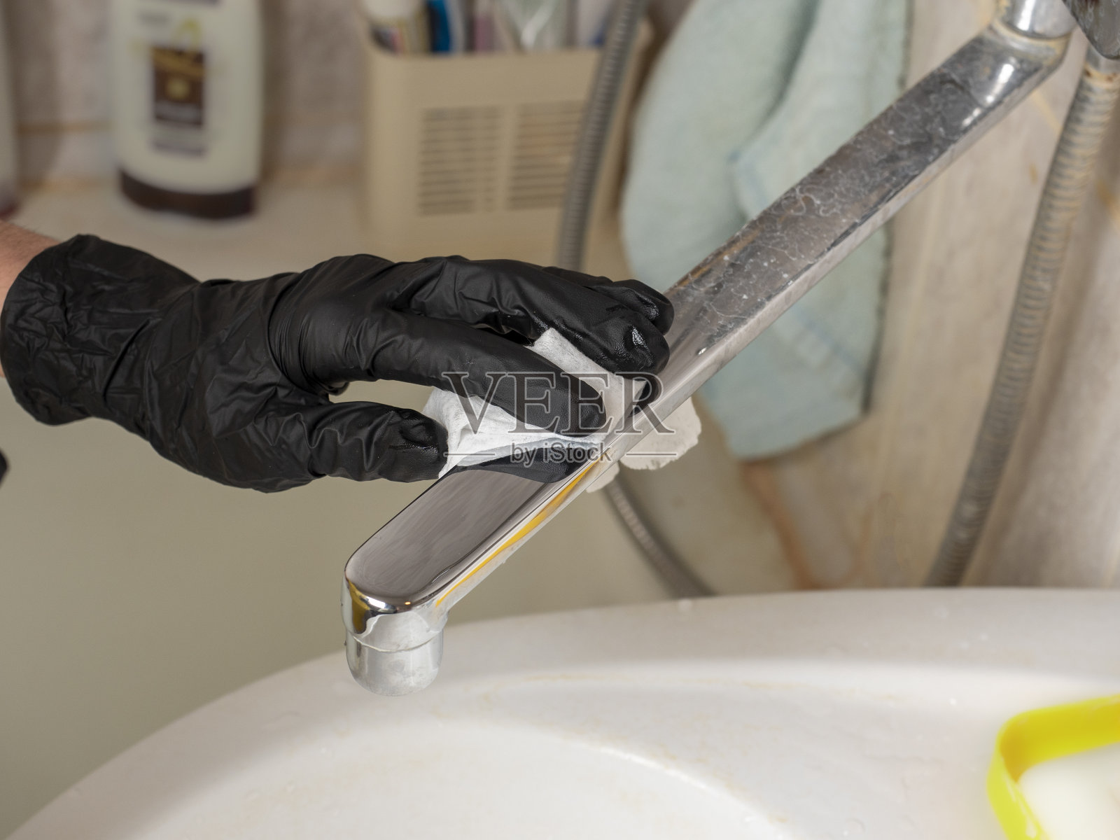 用一块白布清洗浴室的水龙头上的污垢。一只戴着黑色防护手套的手。打扫房间并保持清洁的概念照片摄影图片