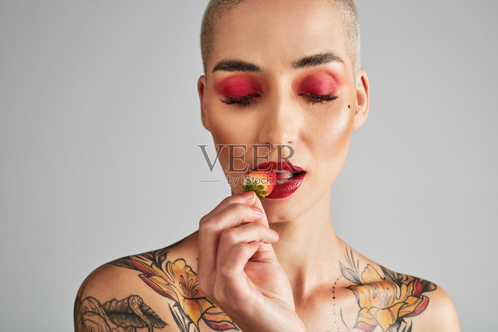 一个美丽的年轻女子在灰色背景下吃草莓的照片照片摄影图片
