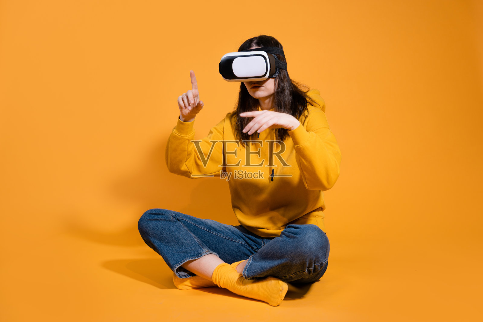 一个黄色背景上带着虚拟现实设备的年轻女子。照片摄影图片