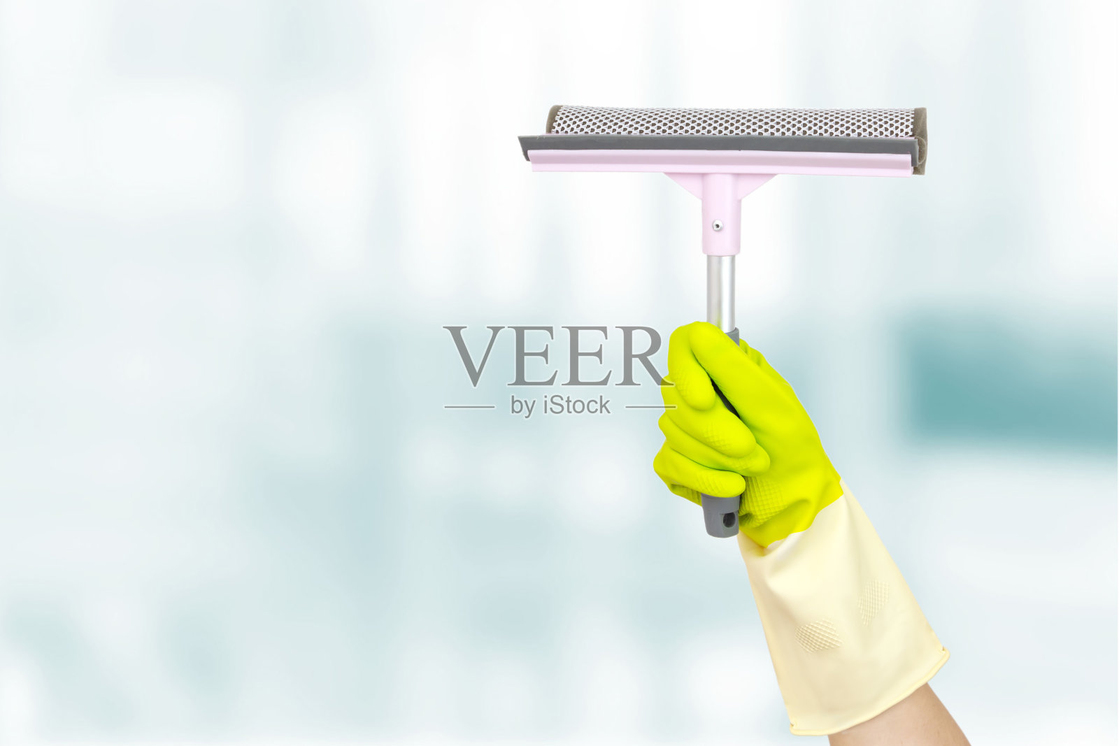 春季大扫除的概念。手里拿着一个粉红色的刮刀,蓝色背景上的窗户。手用擦窗工具。清洁用品的概念。照片摄影图片