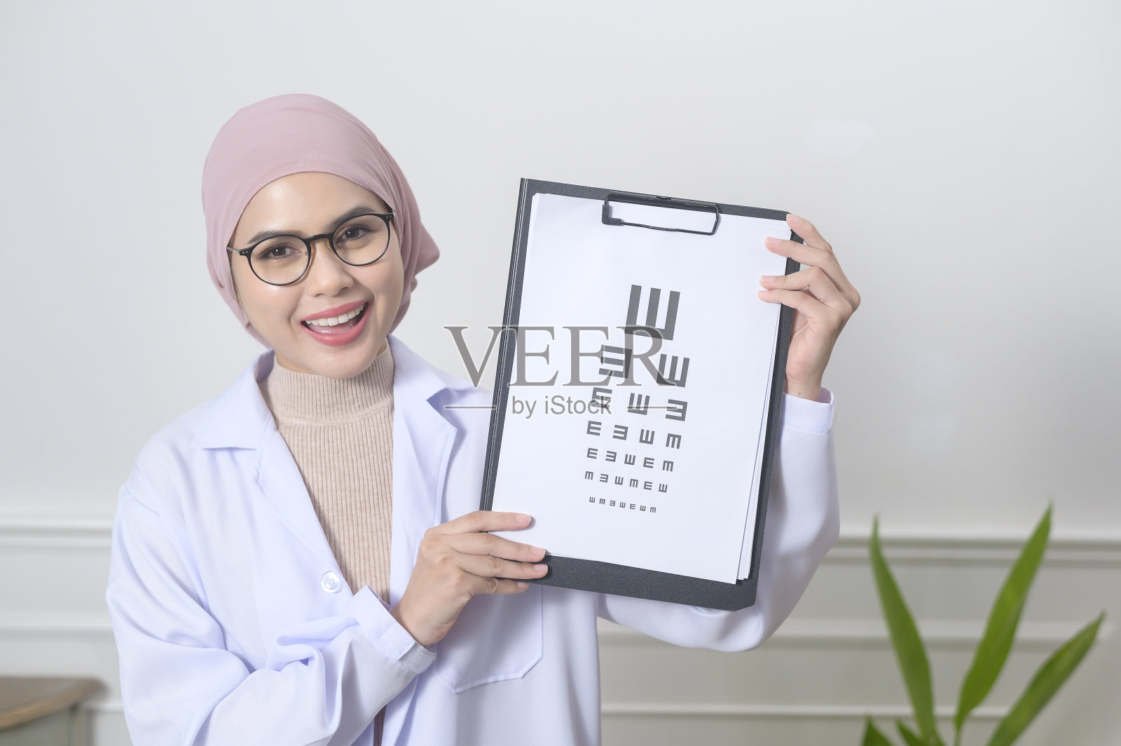 女性穆斯林眼科医生拿着测量视力的视力表测试照片摄影图片