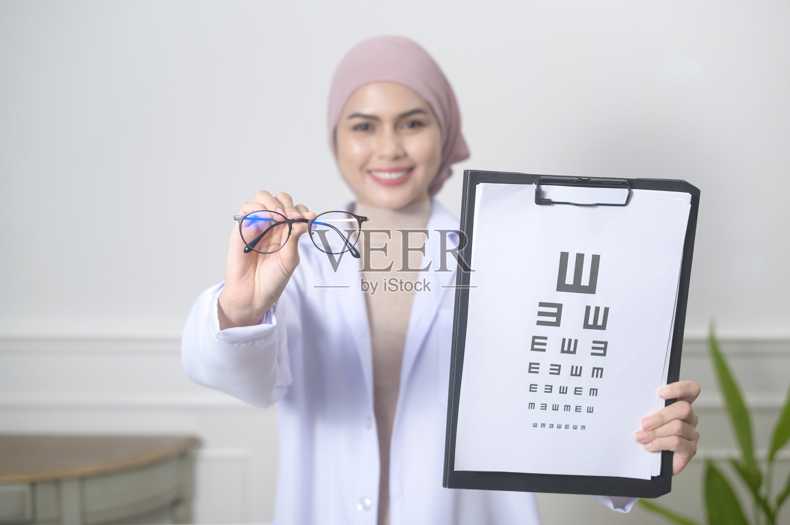 女性穆斯林眼科医生拿着测量视力的视力表测试照片摄影图片