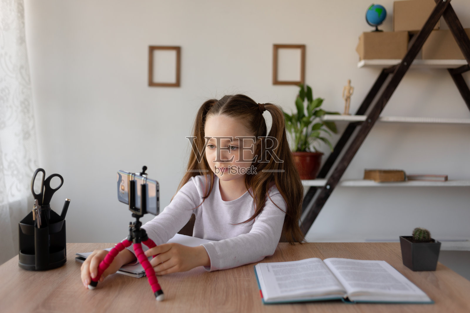 远程学习在线教育。女学生在读一本书。用三脚架上的手机录像。设置一个电话在线学习。照片摄影图片