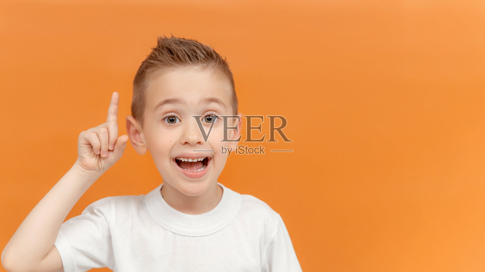 学龄前的小男孩有个好主意。手指指着一个伟大的想法孤立在橙色的背景。特写英俊开朗的小男孩。为你的文本或产品复制空间照片摄影图片
