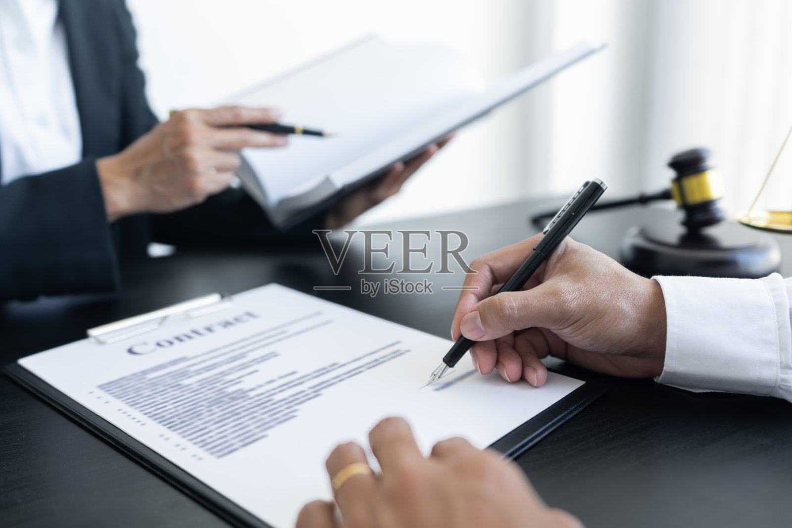 法律上,天秤和锤子放在桌子上,二人正在交易和签订合同,确定法律事项。照片摄影图片