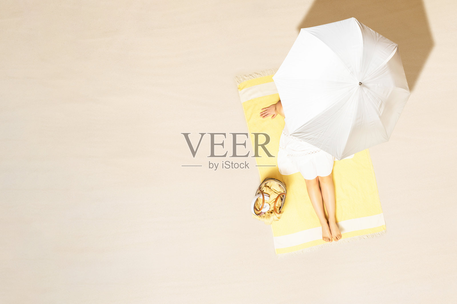 独自女人穿着衣服坐在和日光浴在黄色的沙滩浴巾下伞与包。暑假女性在沙滩上放松。,鸟瞰图照片摄影图片